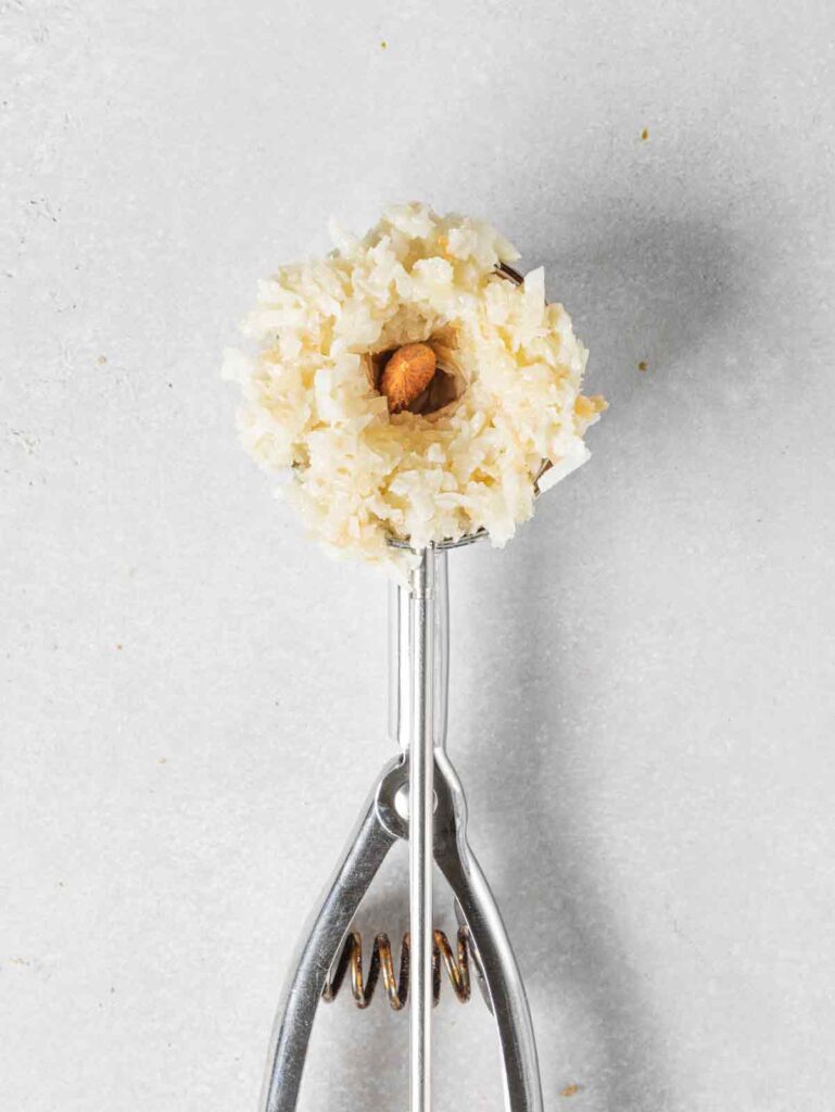 Ice cream scoop with coconut mixture and almond in center.