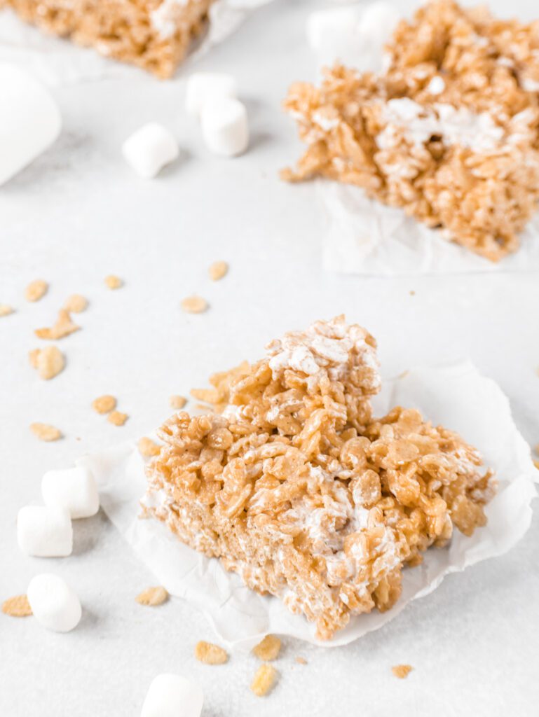 Rice krispie treats on parchment paper with marshmallows and cereal scattered.