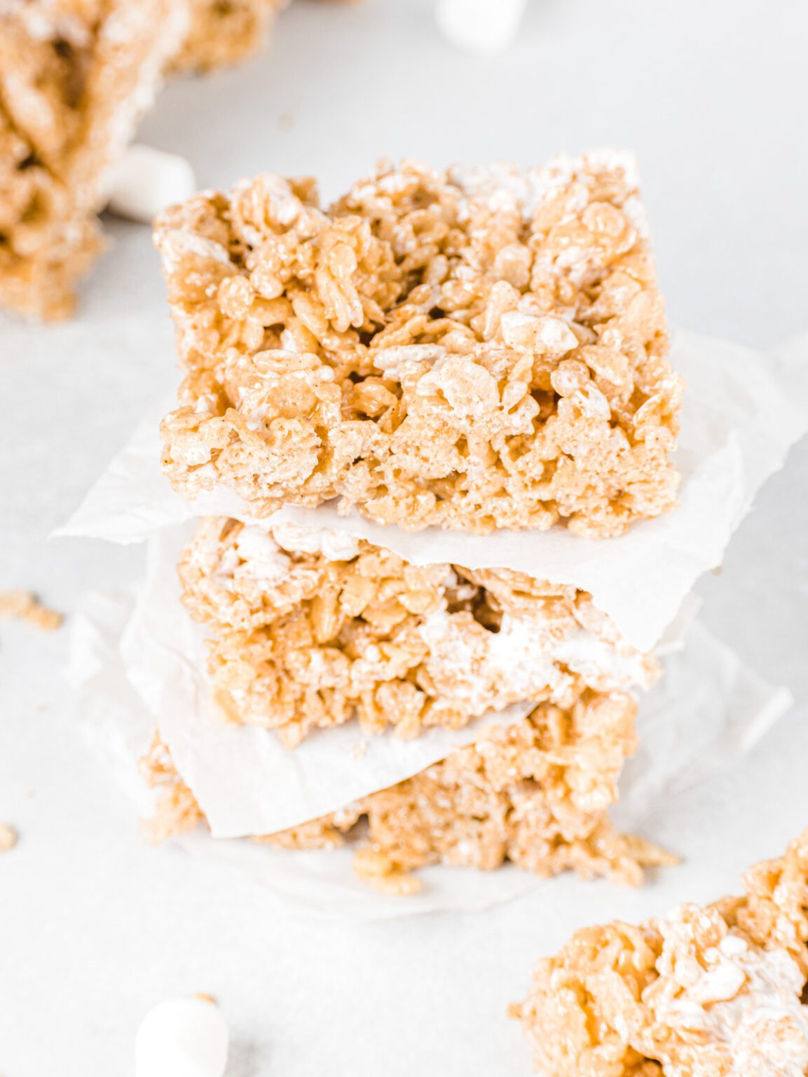 Stack of cereal treats with parchment between and marshmallows scattered.