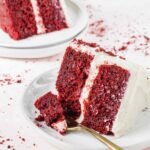 Slice of red velvet cake on plates with fork.