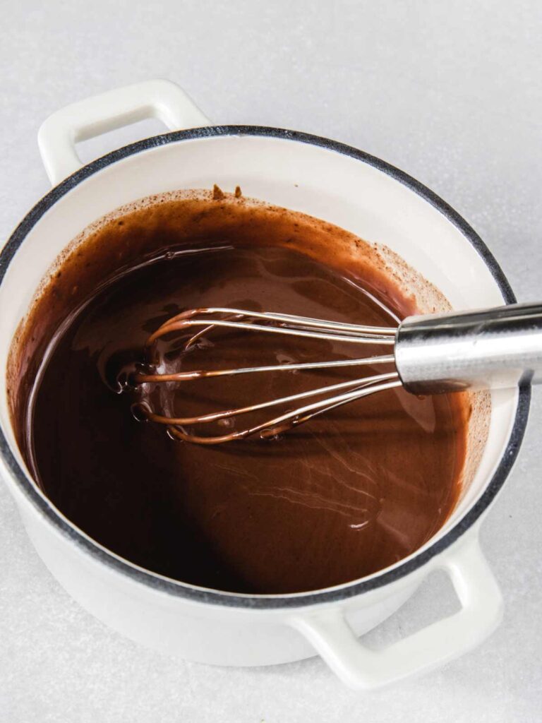 Chocolate ganache in pot with whisk.
