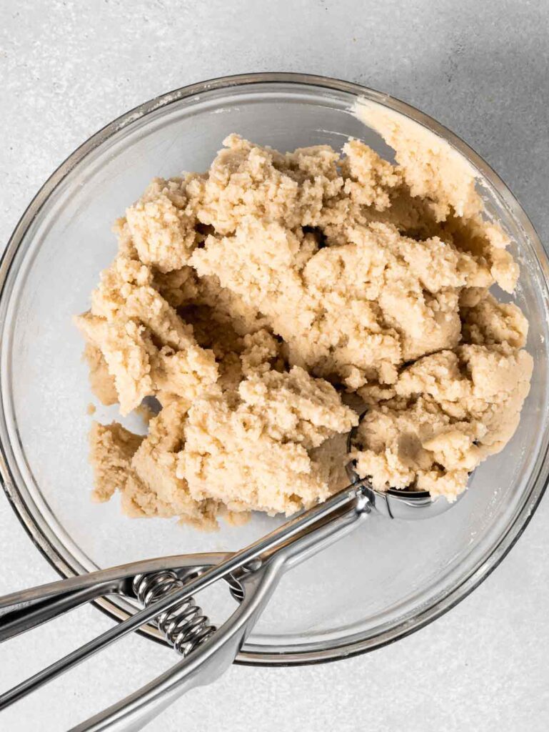 Thumbprint cookie dough in bowl with cookie scoop.