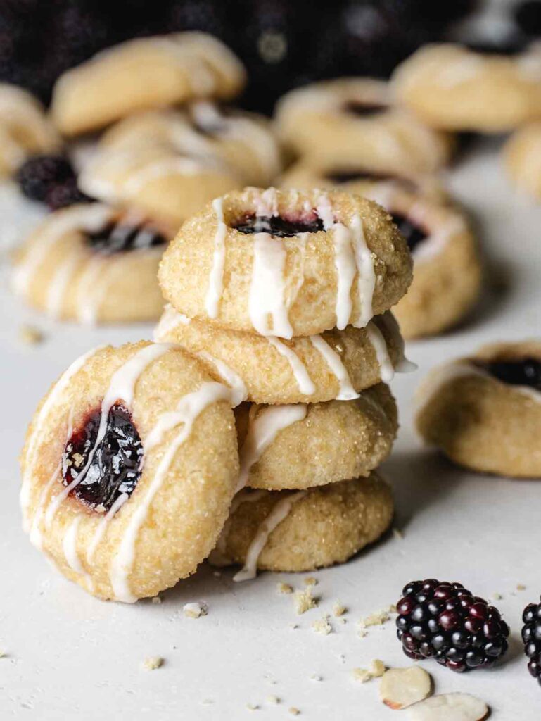 Stack of 4 thumbprint cookies with one on the side and blackberries in the background.