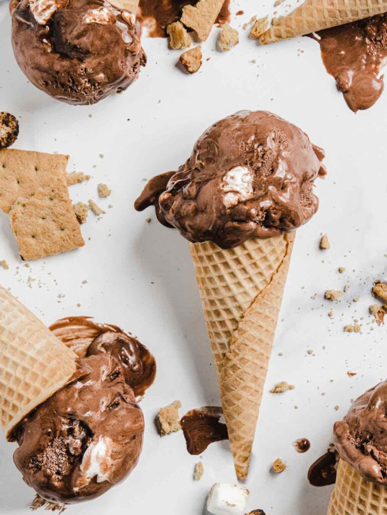 Multiple chocolate ice cream cones on marble with graham cracker crumbs.