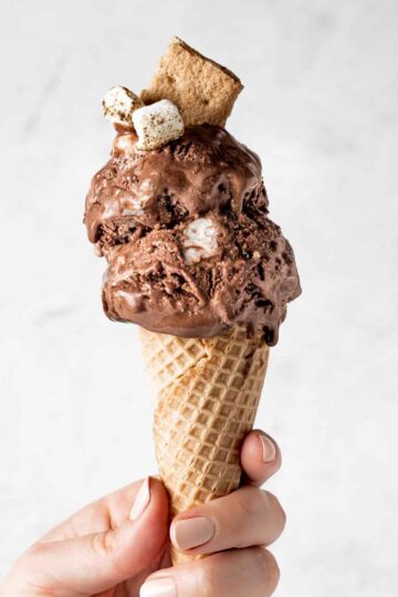 Holding double s'mores ice cream scoop with chocolate ice cream and marshmallow and graham crackers.
