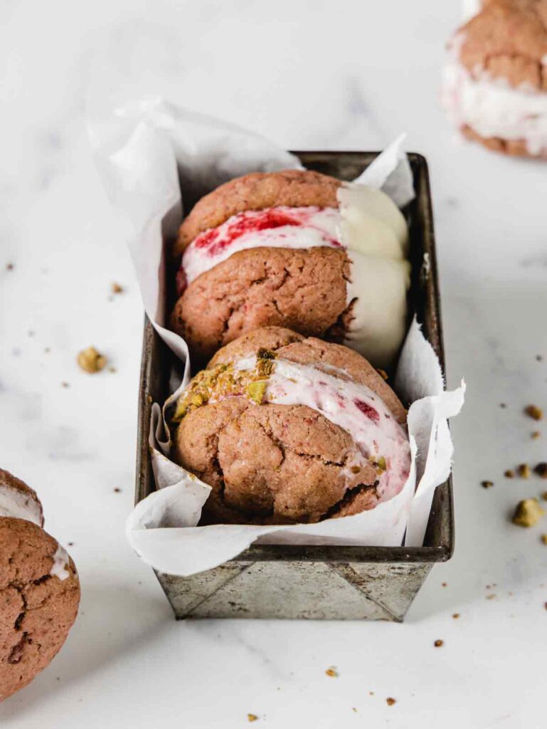 Ice cream sandwiches in pan and two sandwiches sitting on board.