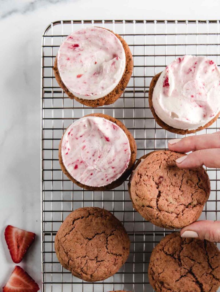 Strawberry cookie top being placed on ice cream sandwich.