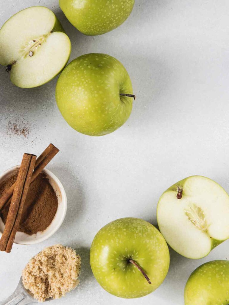 Sliced and whole apples on board with cinnamon and brown sugar.