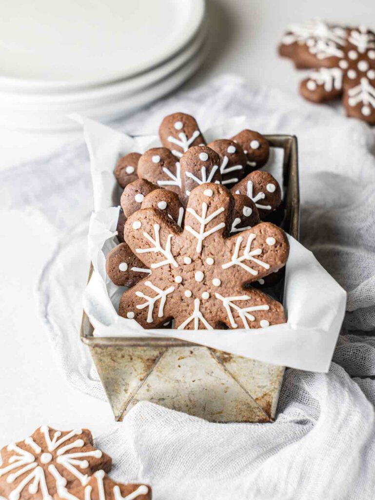 Snowflake cookies in tin with stack of plates.