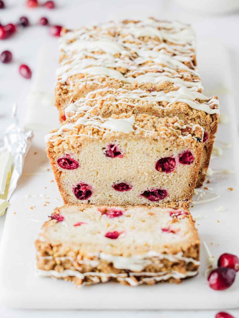 Half sliced cranberry cake on board with fresh cranberries.