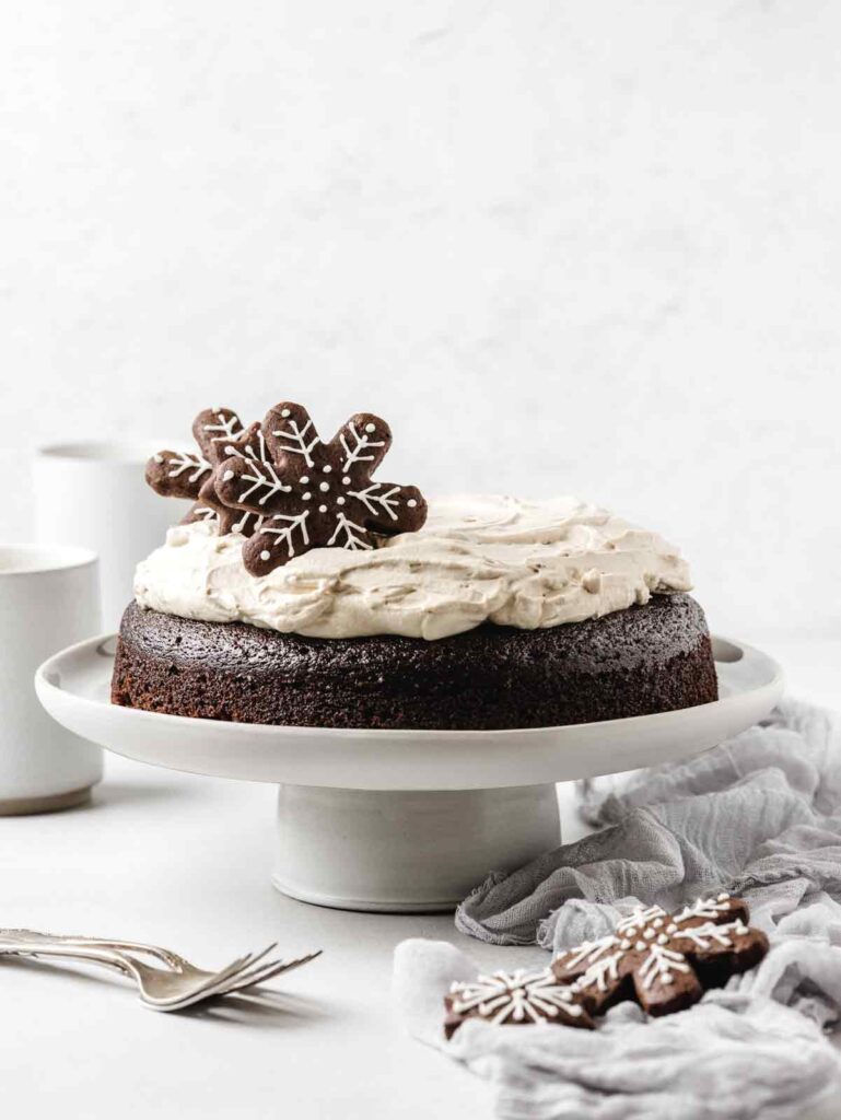 Straight view of gingerbread cake on plate with cookies on top.