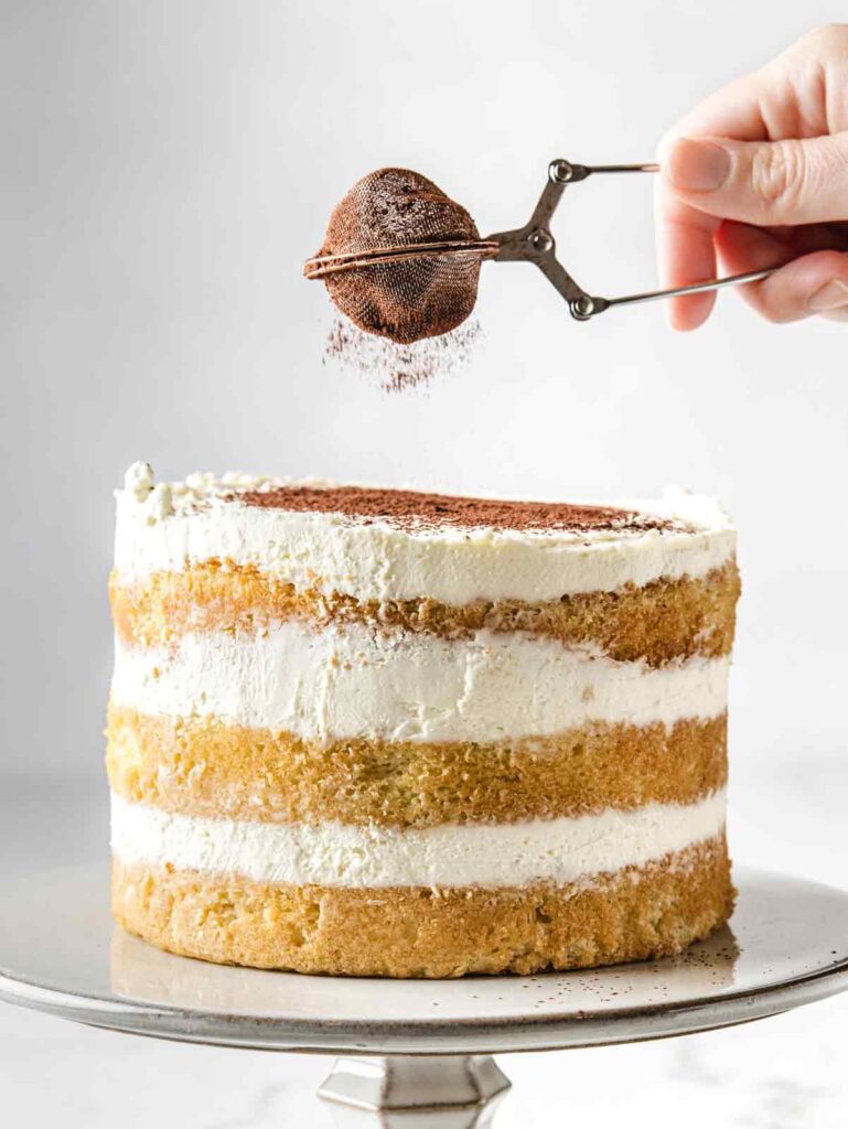 Dusting tiramisu cake with cocoa powder.