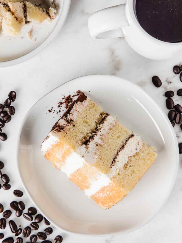 Slice of tiramisu cake on plates with coffee beans and cup.