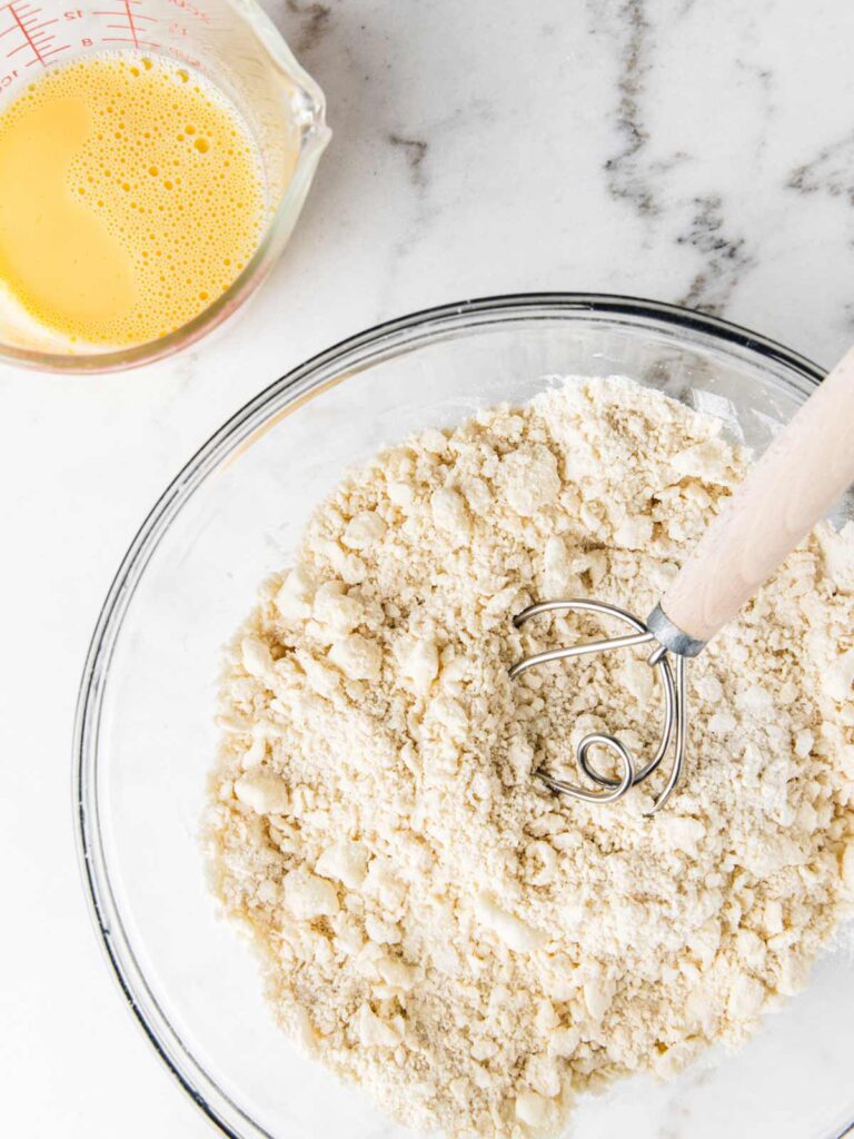 Bowl of flour and pitcher of whisked eggs on board.