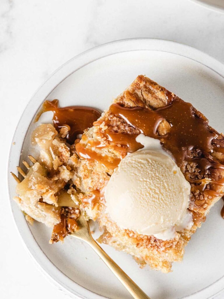 Pie of apple pie bars on plate with fork and ice cream.