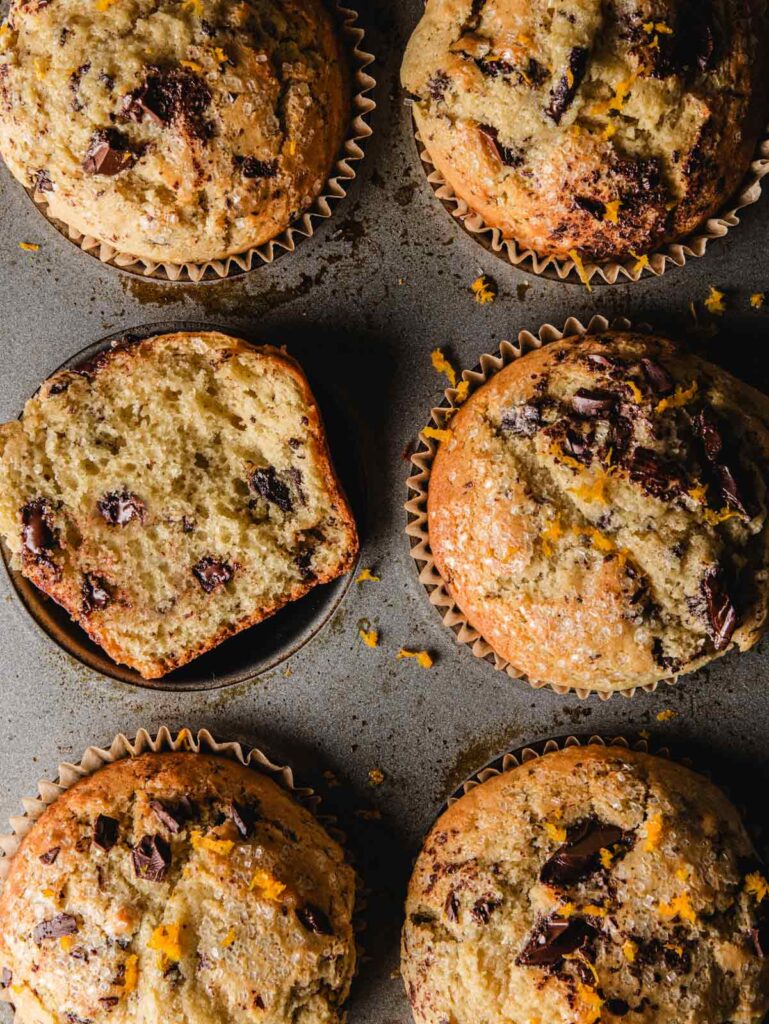 Chocolate and orange muffins in tin with one cut open.