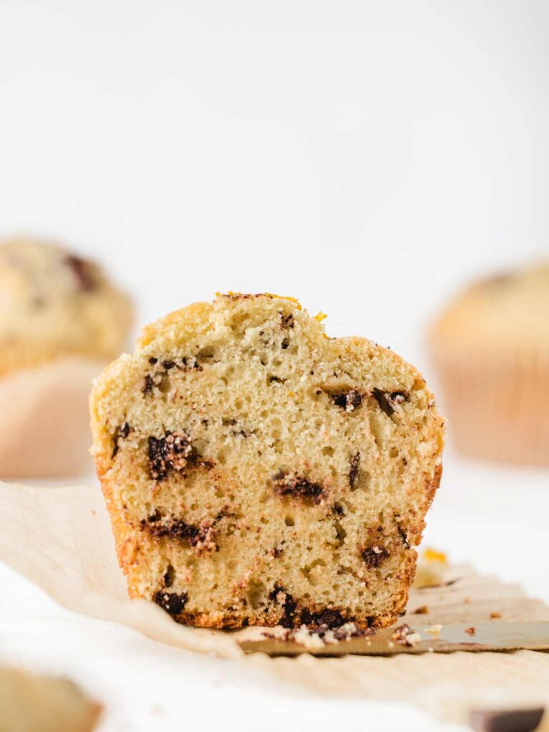 Muffin sliced in half on liner with knife.