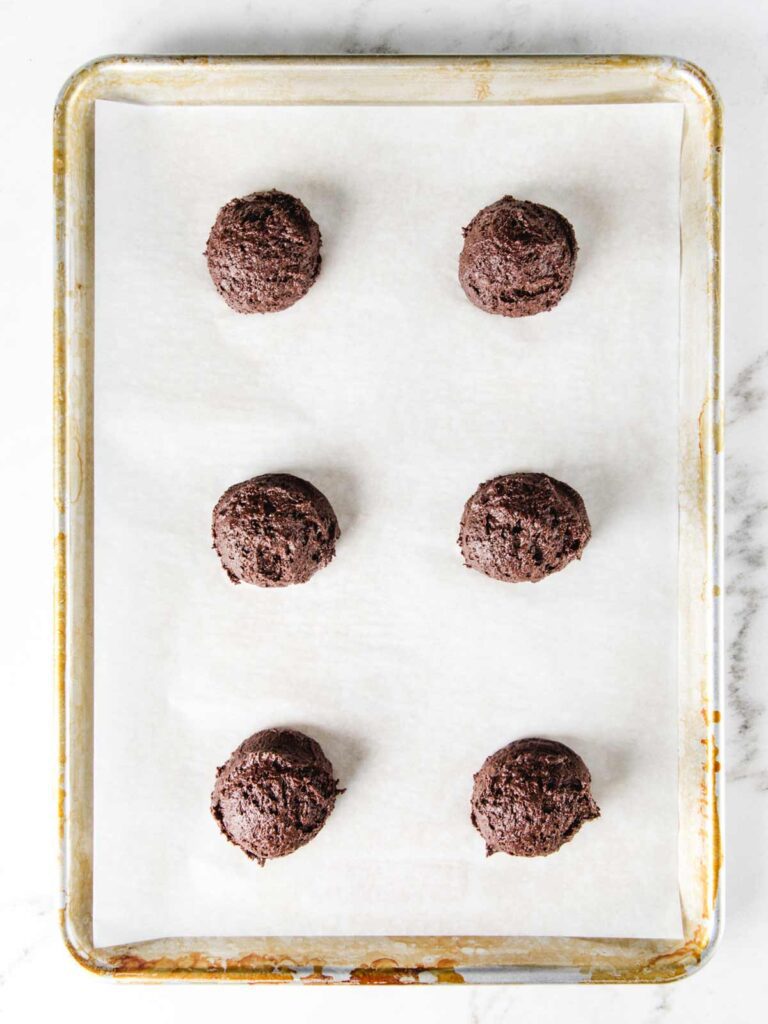 6 unbaked chocolate whoopie pies on sheet pan.