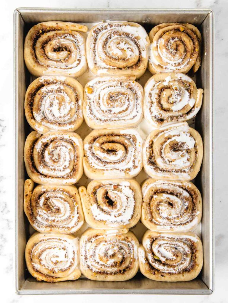 Unbaked rolls in sheet pan with heavy cream on top.