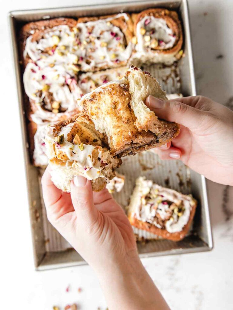 Pulling apart cinnamon roll in front of baking sheet.