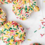Sprinkle covered cookies on parchment paper with bite missing.