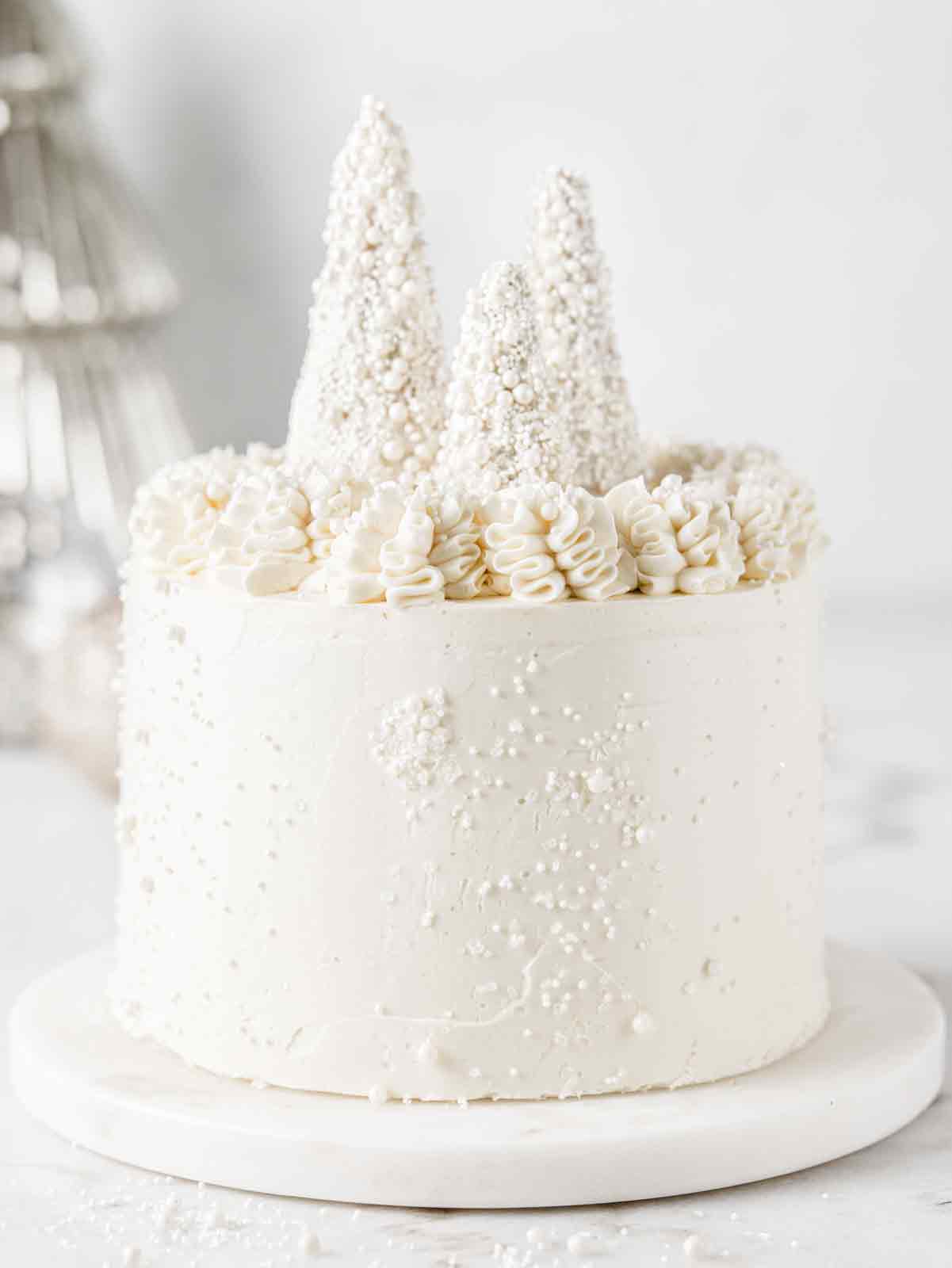 White cake on marble board with glittery trees on top.