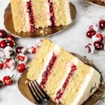 Two slices of orange cake on plates with fork and sugared cranberries around.