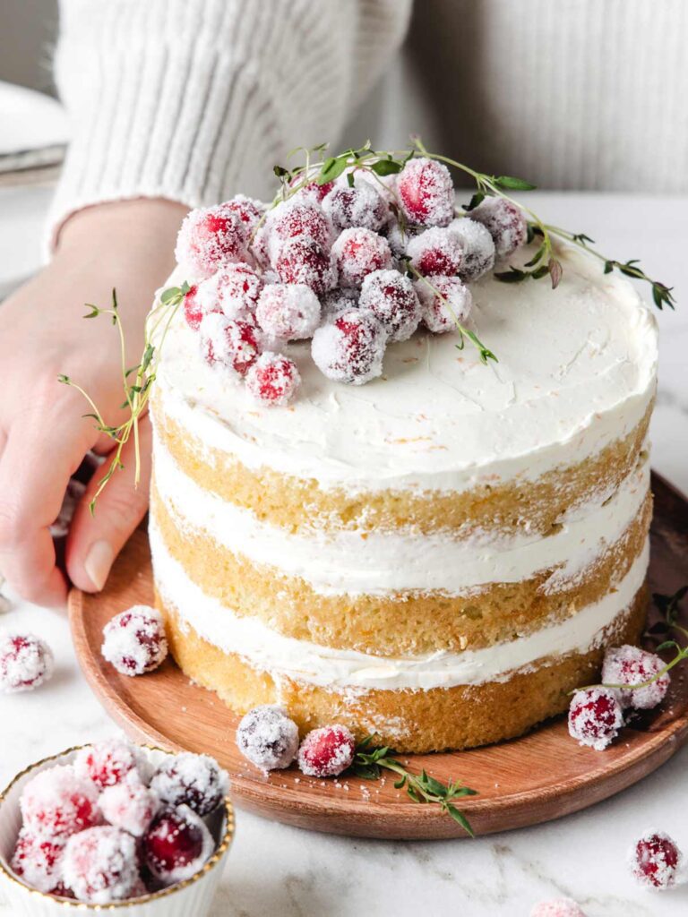 Person setting layer cake on table with sugared cranberries on top.