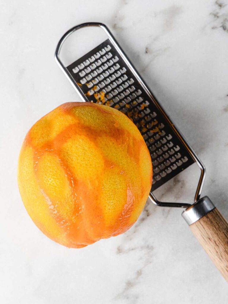 Zested orange with zester on table.