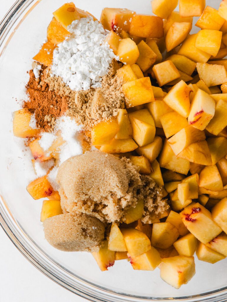 Diced peaches in bowl with spices and sugar on top.