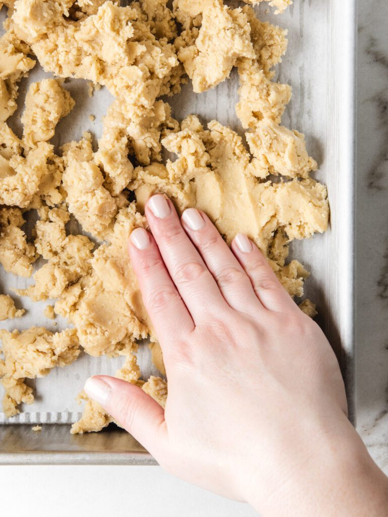 Fingers patting shortbread dough into layer.