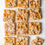 Sliced squares of peach bars on board with bite taken from one square.