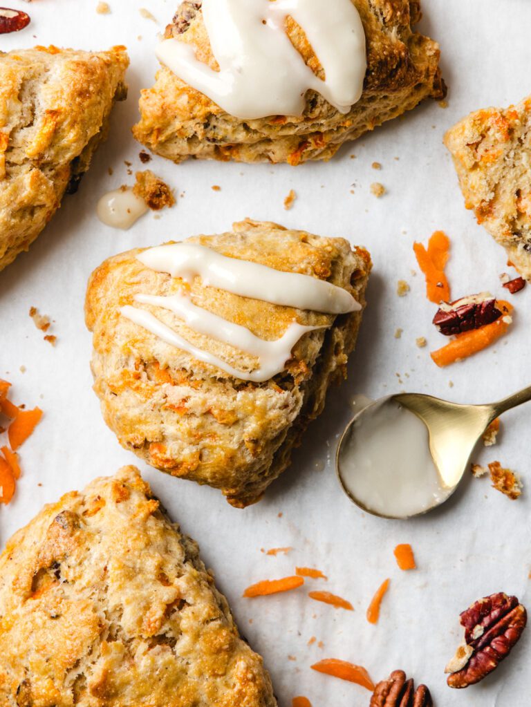 Scones on table with scattered carrots and glaze on spoon.