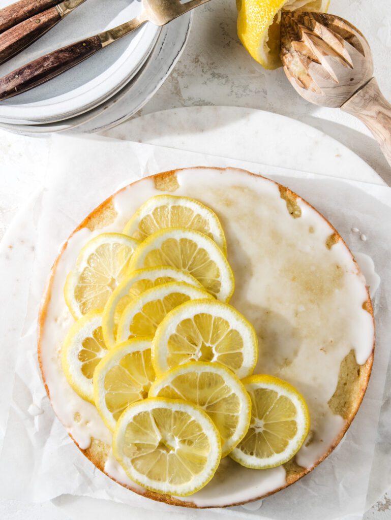 Cake with lemon slices with plates stacked and lemon zester.