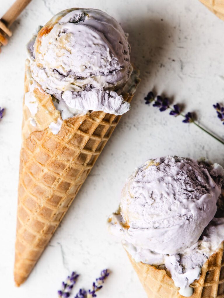Two ice cream cones on table with honey and lavender on the side.