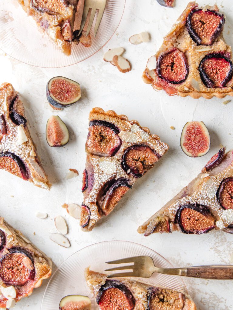Slices of tart with figs on top on pink plates.