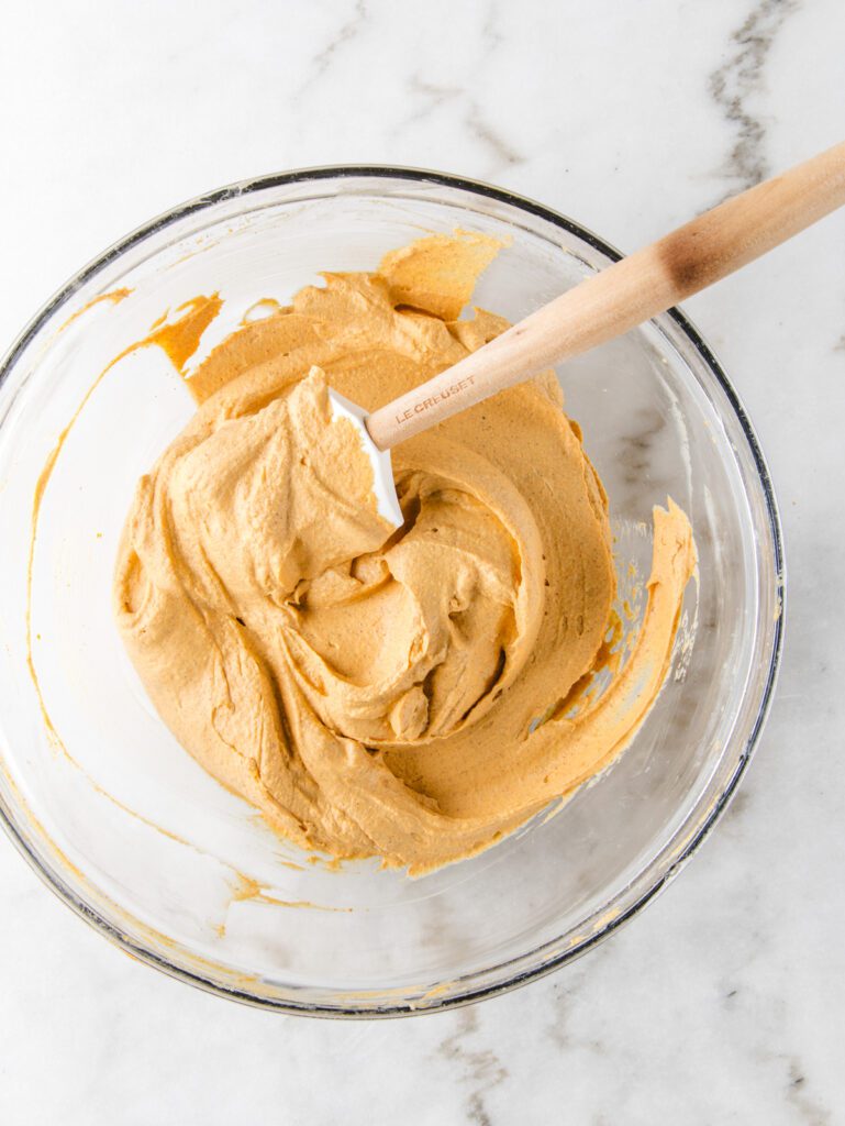 Glass bowl with pumpkin pie filling and spatula.