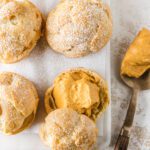 Cream puffs on board with one sliced open with filling.