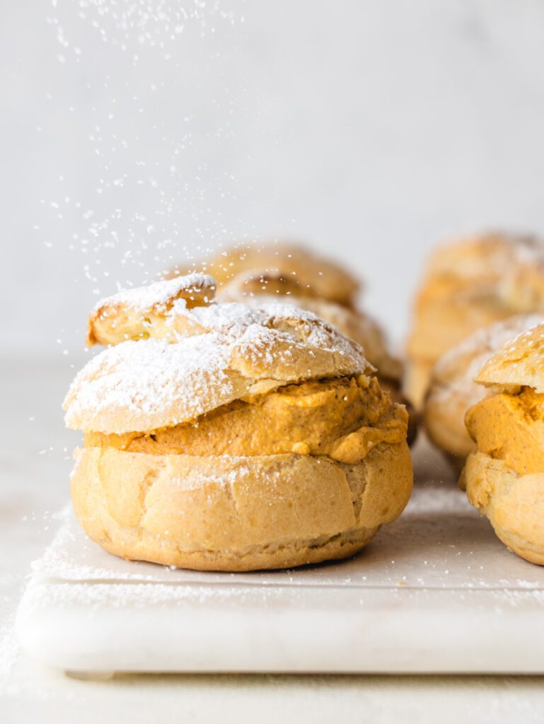 Cream puff on table with pumpkin filling with sugar sprinkling on top.