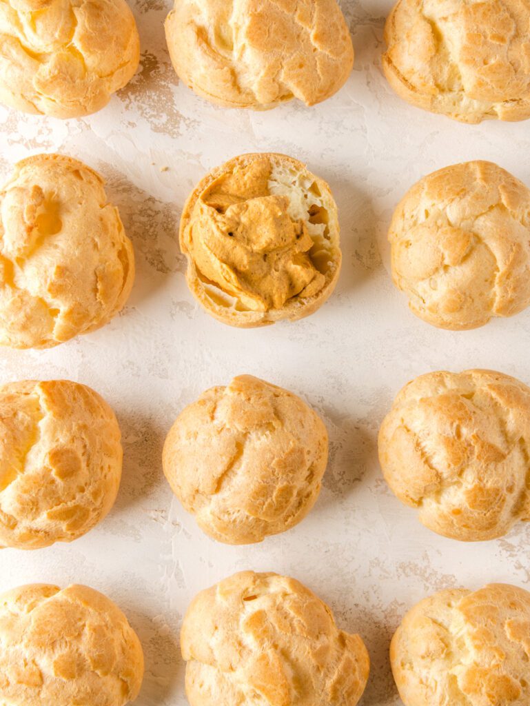 Rows of 12 cream puffs on table, one cut open with pumpkin filling inside.