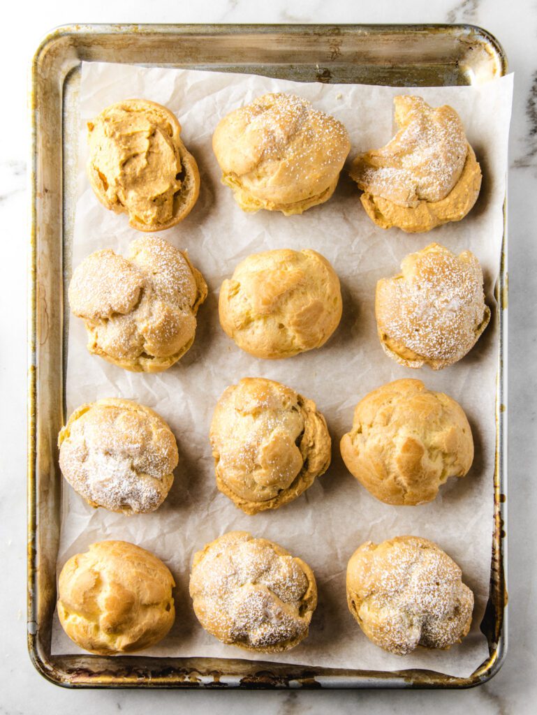 Baking sheet filled with pumpkin cream puffs with confectioners' sugar on top.