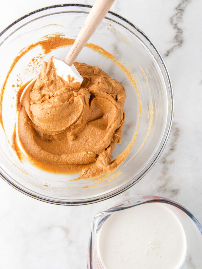 Whipped pumpkin in glass bowl with measuring cup of cream on side.