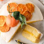 Cake sliced on marble with oranges on top.