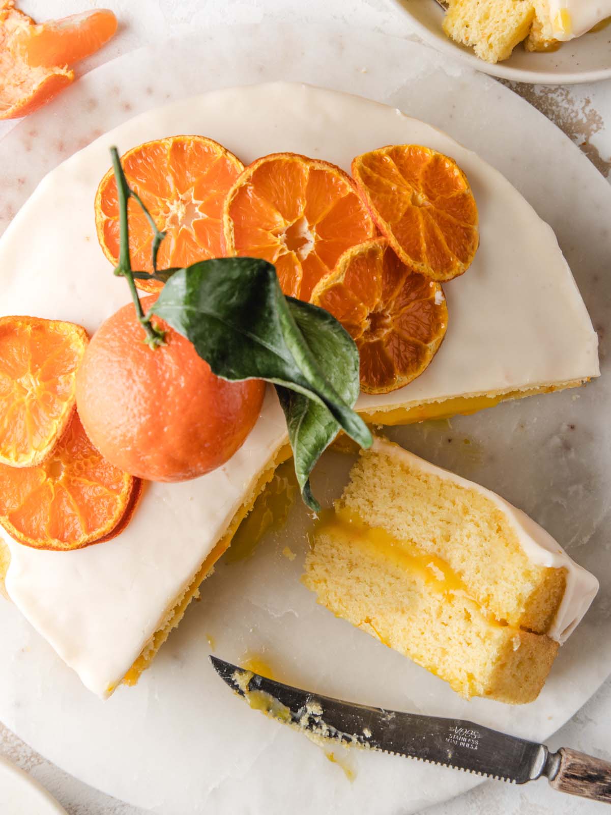 Cake sliced on marble with oranges on top.