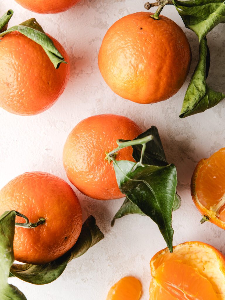 Mandarin oranges on table with stems and leaves.