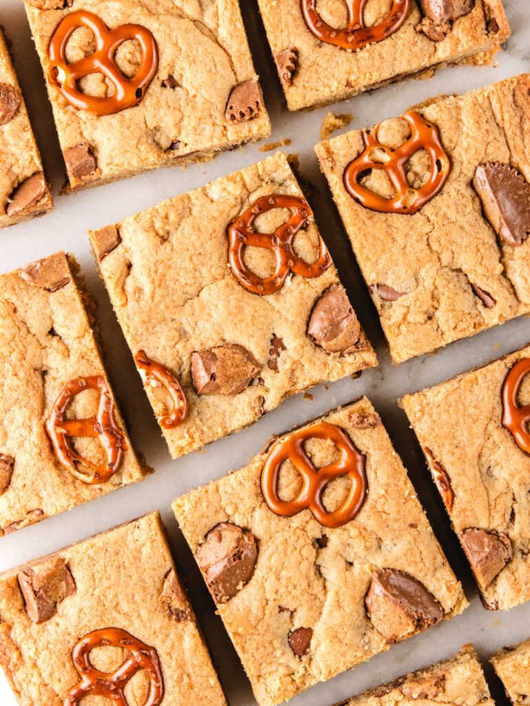 Rows of blondies on marble with pretzels and chocolate on top.