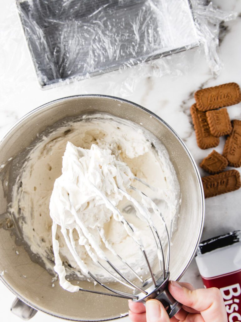 Whipped cream in mixer with cookies scattered beside.