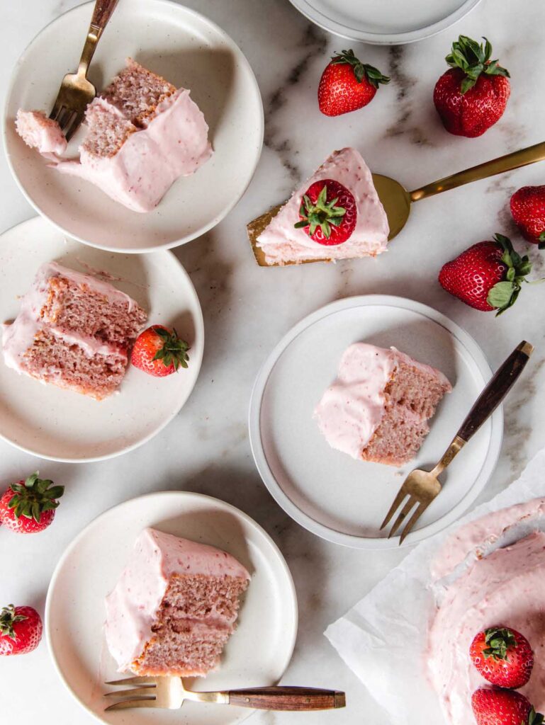 Plates scattered on table with pink cake and strawberries.
