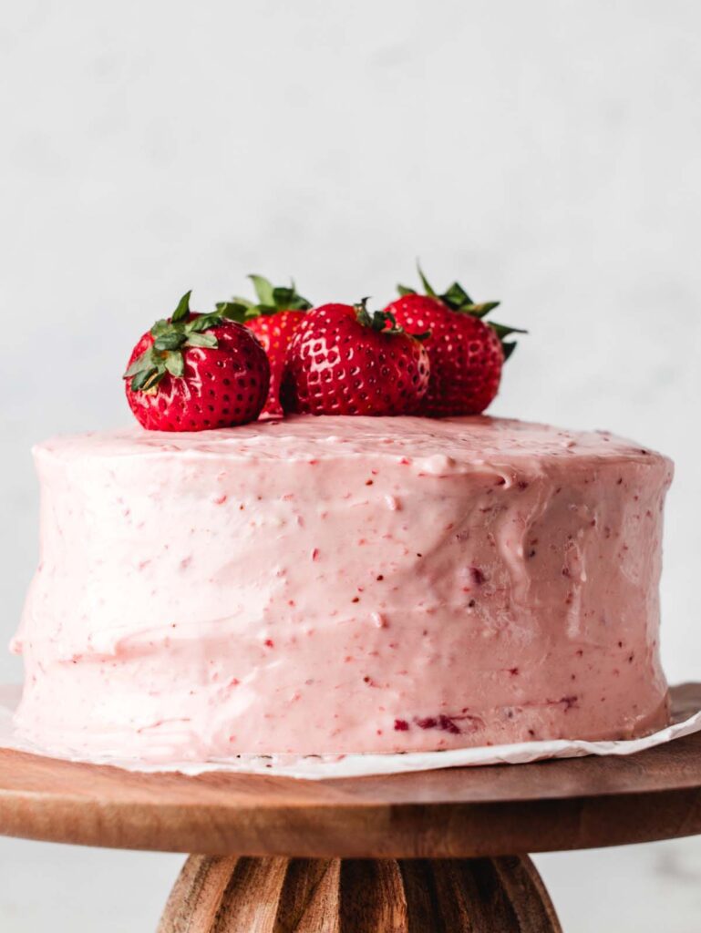 Strawberry cake on cake stand with fresh berries on top.
