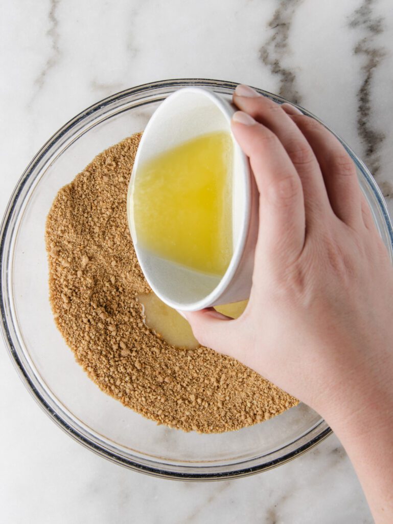Pouring melted butter in bowl of cookie crumbs.